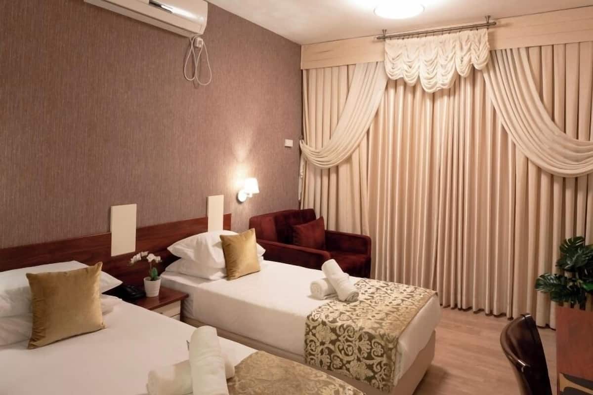 A hotel room with two beds, a sofa, a desk, and a potted plant.