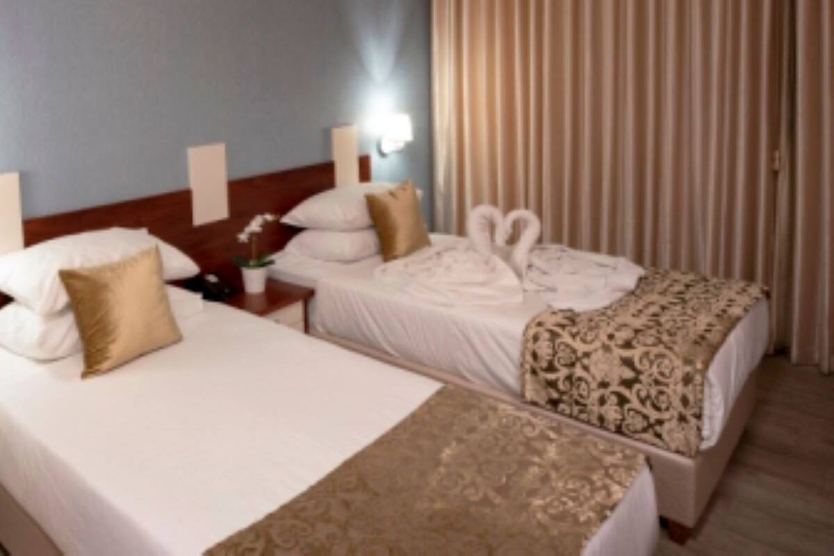 A hotel room with two beds, a nightstand with a lamp, and a large window with curtains.