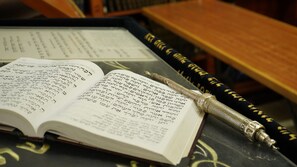 An open book with Hebrew text, a pen, and a decorative object on a table. - Aristocrat Hotel (Bene Beraq)