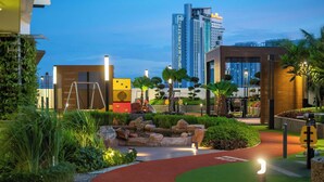 A landscaped outdoor area with a red pathway, greenery, and modern buildings in the background. - (Kids Fun) 2BR Space Apt near KSL CIQ JB (Johor Bahru)
