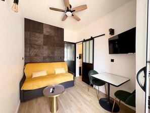 A modern living room with a sofa, a small round table, a ceiling fan, and a TV mounted on the wall. - La Villa Bligny  (Étretat)