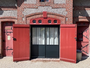 Um portão de metal vermelho com uma porta preta, embutido em um edifício de tijolos com detalhes decorativos.
