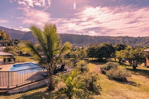 A pool with a surrounding deck, palm trees, and a mountainous backdrop.