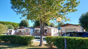 A row of mobile homes with wooden decks and railings, surrounded by greenery and a clear sky. - Mobile Home in Sarazena in Einem Ferienpark (Sarzana)