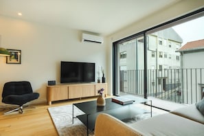 Uma sala de estar moderna com televisão de tela plana, sofá, mesa de centro e varanda com vista para prédios.