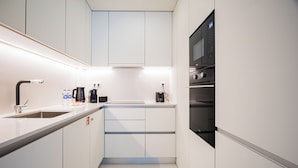 Une cuisine moderne avec des meubles blancs, un four noir et une machine à café.
