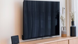 Un salon moderne avec un téléviseur à écran plat fixé à un meuble en bois, un canapé noir et une table à manger en bois.