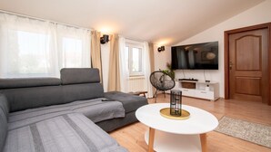 Ein modernes Wohnzimmer mit einem grauen Sofa, einem weißen Couchtisch, einem Fernseher auf einem weißen Schrank und einer Holztür.