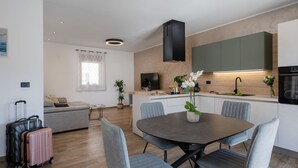 A modern kitchen with a central island, a dining area with a table and chairs, a sofa, and a TV. There is a window with a curtain and a plant on the island. - Kuca za odmor Hana by Villas Guide (Vodnjan)