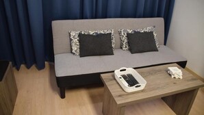 Moderni olohuone, jossa on harmaa sohva, kaksi kuviollista koristetyynyä, puinen sohvapöytä ja kori, jossa on kaukosäädin.