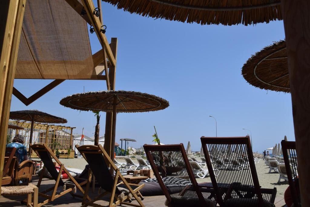Un salon de plage avec des chaises en bois et des parasols en chaume, offrant une vue sur la mer.