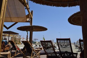 A beachside lounge with wooden chairs and thatched umbrellas, overlooking the sea. - Comfortable 1-Bed Apartment in Beachfront Block, Ideal Location (Larnaka)