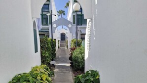 En sti omkranset af frodig vegetation, der fører til en bygningsindgang med en markant hvid facade og buer.