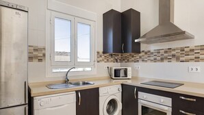 Une cuisine compacte équipée d’un lave-vaisselle, d’une machine à laver, d’un four à micro-ondes, d’un four traditionnel et d’une grande fenêtre.