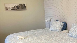 A neatly made bed with a patterned bedspread, two pillows, and a rolled towel on the side.