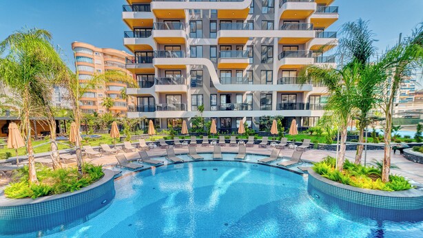 Um hotel moderno com área de piscina, espreguiçadeiras e palmeiras.