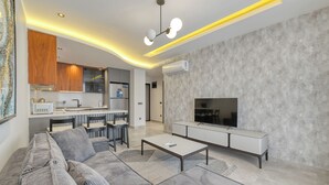 Uma sala de estar moderna com sofá, mesa de centro, televisão e área de cozinha.