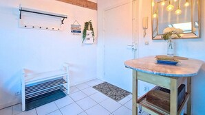 Une salle de bain avec un banc blanc, une étagère en bois, un miroir avec des lampes suspendues et un sol carrelé.