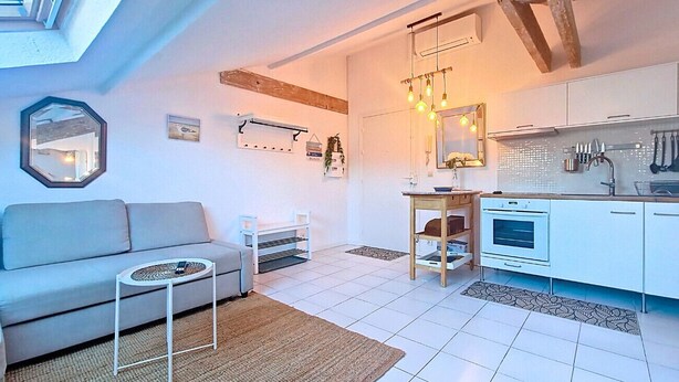 Un salon moderne comprenant un canapé, une petite table ronde et un coin cuisine avec des placards et un plan de travail.