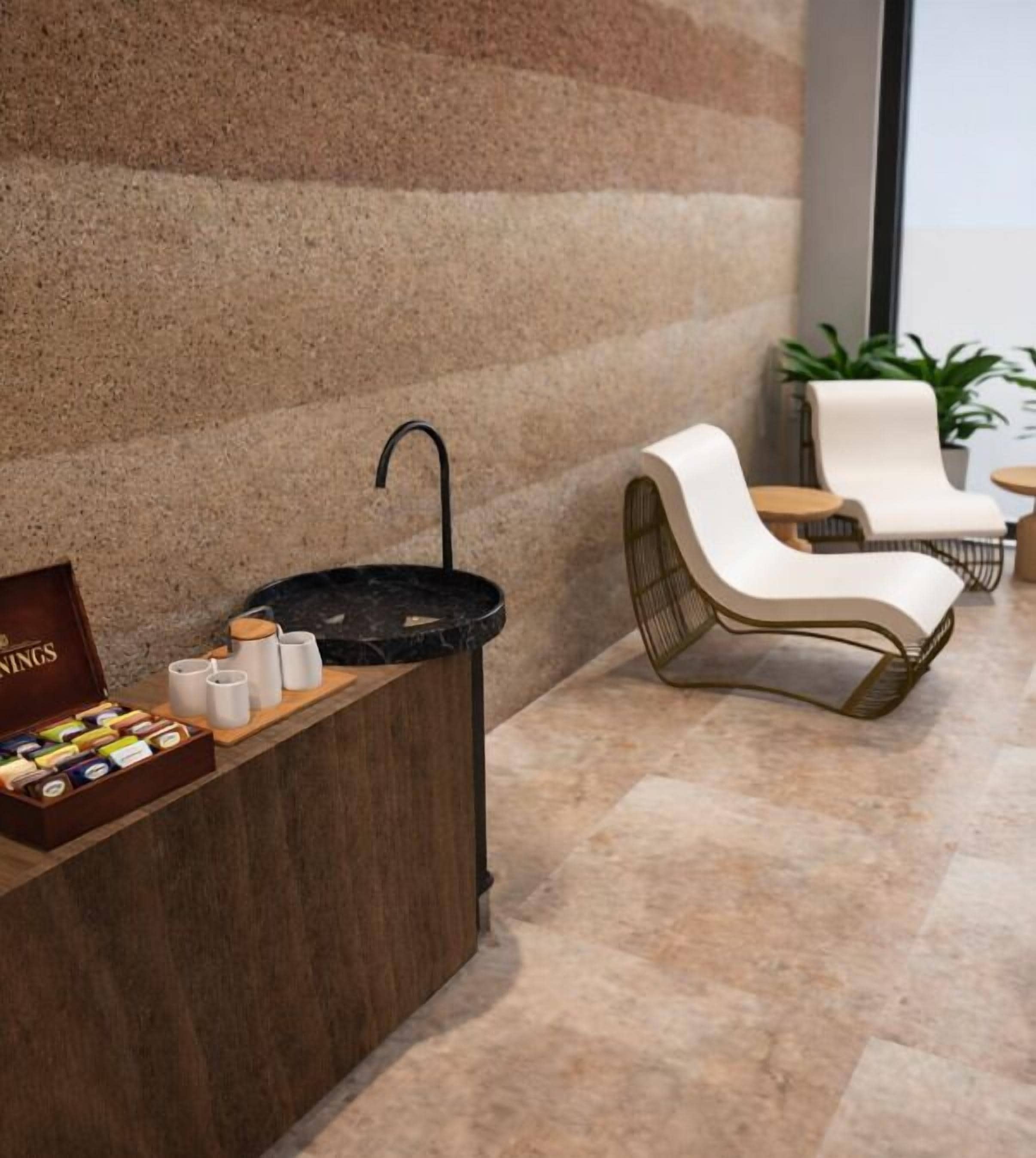 A reception area with a marble counter, a black sink, and a wooden box of chocolates. There are two white chairs and a small table with a plant.
