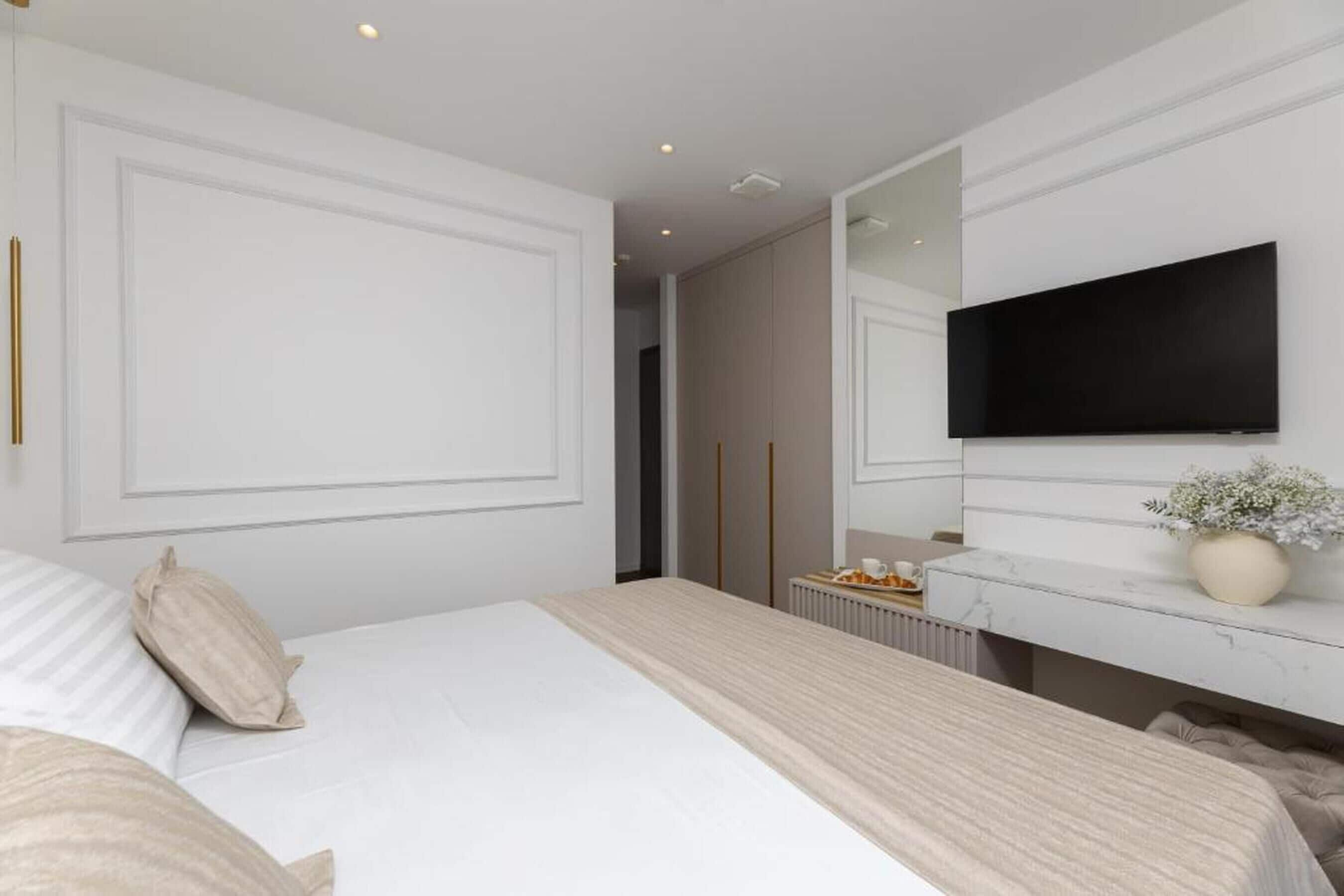 A modern bedroom with a large bed, a mounted TV, a vanity with a mirror, and a radiator.