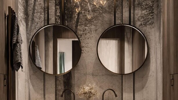 A modern bathroom with two round mirrors, a central chandelier, and a marble floor.