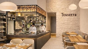 A restaurant interior with a bar area, seating, and a stone wall with the name 'Tessera' on it.