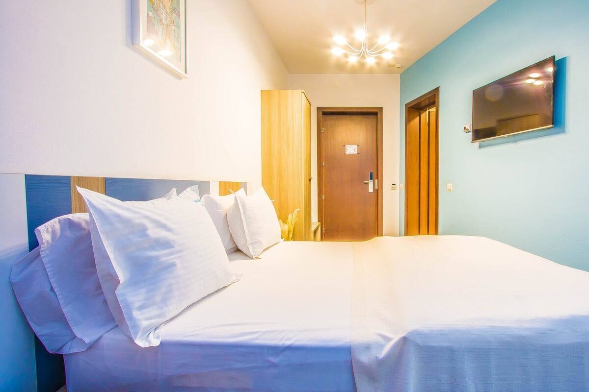 Ein Hotelzimmer mit einem Bett, einer Holztür und einer hellblauen Wand.