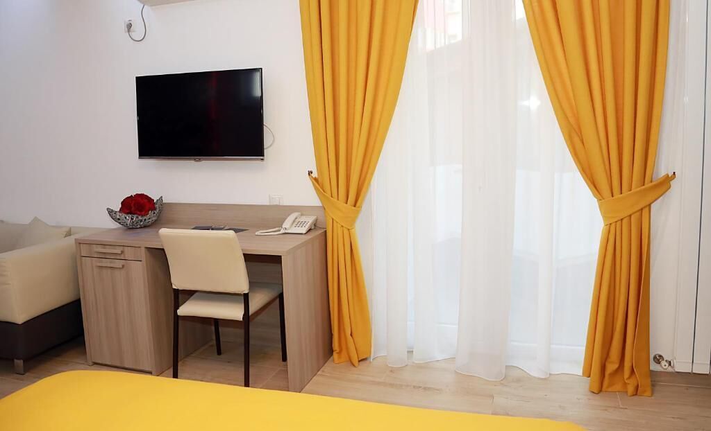 Una habitación de hotel con cama, escritorio, silla, televisor y cortinas amarillas.