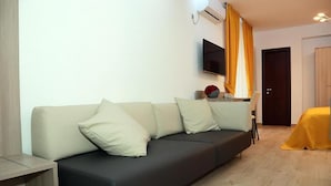 A modern living room with a sofa, a TV mounted on the wall, and a door in the background.