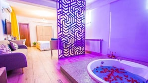 A modern hotel room with a large bed, a sofa, a decorative partition, and a bathtub with rose petals.
