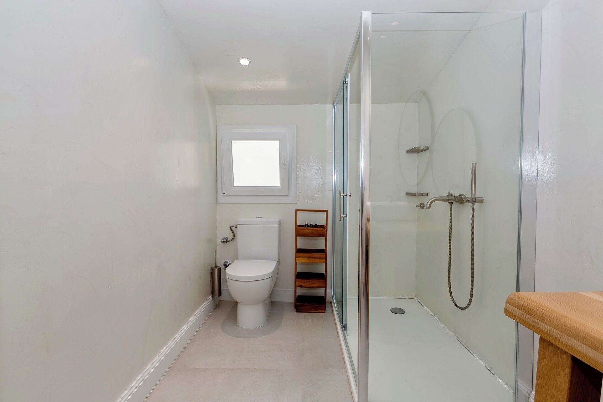 A modern bathroom with a glass-enclosed shower, a toilet, and a small window.