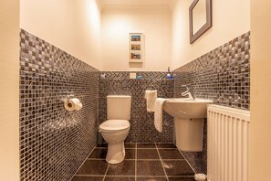 A small bathroom with a toilet, sink, and tiled walls. - Links Lodge | Blacklaws Steading (Anstruthe)