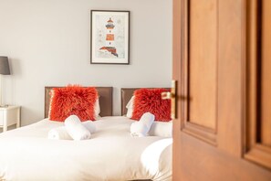 A neatly made bed with white linens and two red pillows, a framed artwork on the wall, and a wooden door partially open. - Links Lodge | Blacklaws Steading (Anstruthe)