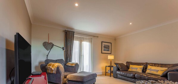 A living room with a sofa, armchair, and a flat-screen TV. - Links Lodge | Blacklaws Steading (Anstruthe)
