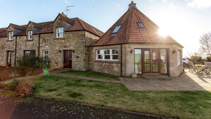 Une maison en pierre avec un toit en tuiles, un petit garage attenant et une pelouse bien entretenue.