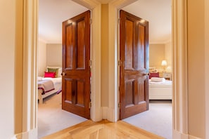 Una habitación de hotel con piso de madera, una cama con cabecera blanca y una mesita de noche con lámpara.