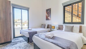 A hotel room with two beds, a large window with bars, a painting on the wall, and a view of buildings outside. - Residence 4 - Apartments in Mar Mikhael (Beirut)