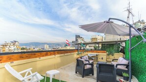 A rooftop terrace with outdoor furniture, a flag, and a view of the city. - Residence 4 - Apartments in Mar Mikhael (Beirut)