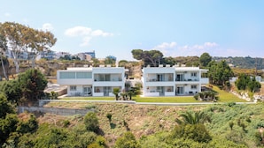 Un edificio residencial moderno de dos pisos con techo plano, ventanas amplias y un jardín bien cuidado.