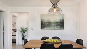 Un comedor con una mesa de madera, sillas negras y un frutero. Hay un cuadro en la pared y una planta en la esquina.