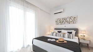 Une chambre moderne avec un grand lit, une literie blanche, un ensemble d’oreillers à rayures, un climatiseur mural et une œuvre d’art sur le thème du bambou.