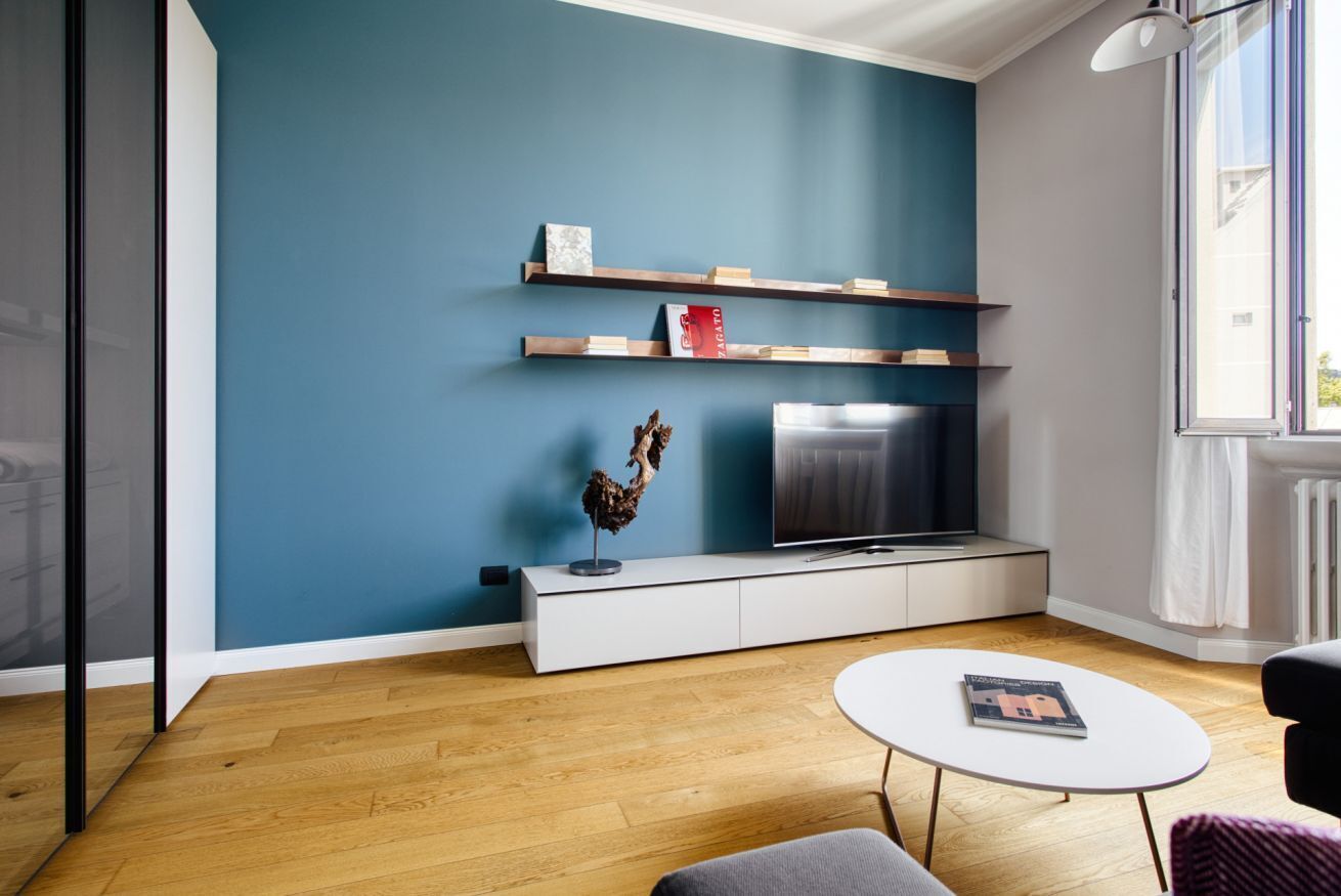 Un salon moderne avec un mur d’accent bleu, un téléviseur à écran plat, des étagères en bois et une table basse blanche.