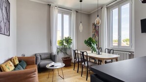 Ett modernt vardagsrum med en soffa, ett matbord, stolar, ett soffbord och stora fönster med gardiner.