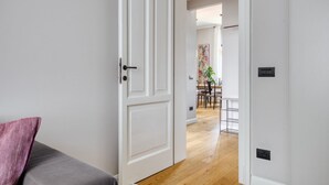 En hall med en vit dörr, en grå soffa och en matplats i bakgrunden.