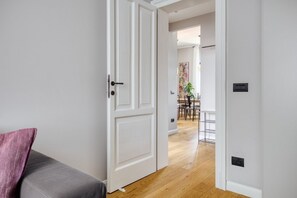 A hallway with a white door, a gray sofa, and a dining area in the background. - Hostmate - Milano - Viale Zara  (Milano)