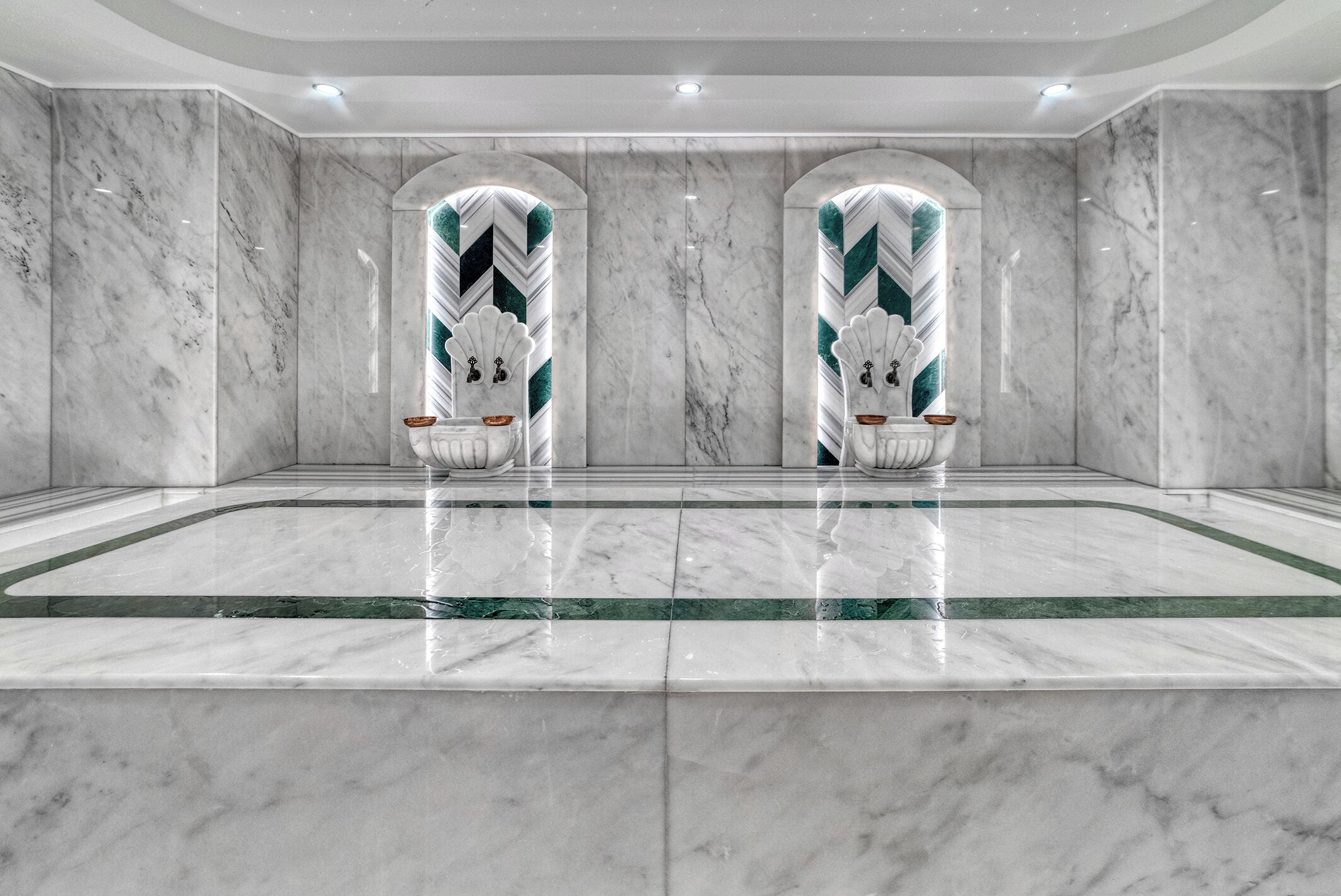 Een ruime lobby met marmeren vloer, met twee boogvormige nissen versierd met decoratieve schelpen en groene accenten.