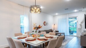 Un comedor moderno con una mesa de vidrio, sillas color beige y una lámpara de araña.