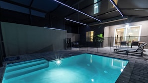 Una piscina interior moderna con superficie de agua cristalina, rodeada por un patio de ladrillo y un área de estar cubierta con una mesa y sillas.