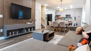 Una sala de estar moderna con un televisor de pantalla plana, un sofá gris y un comedor con sillas y una mesa.